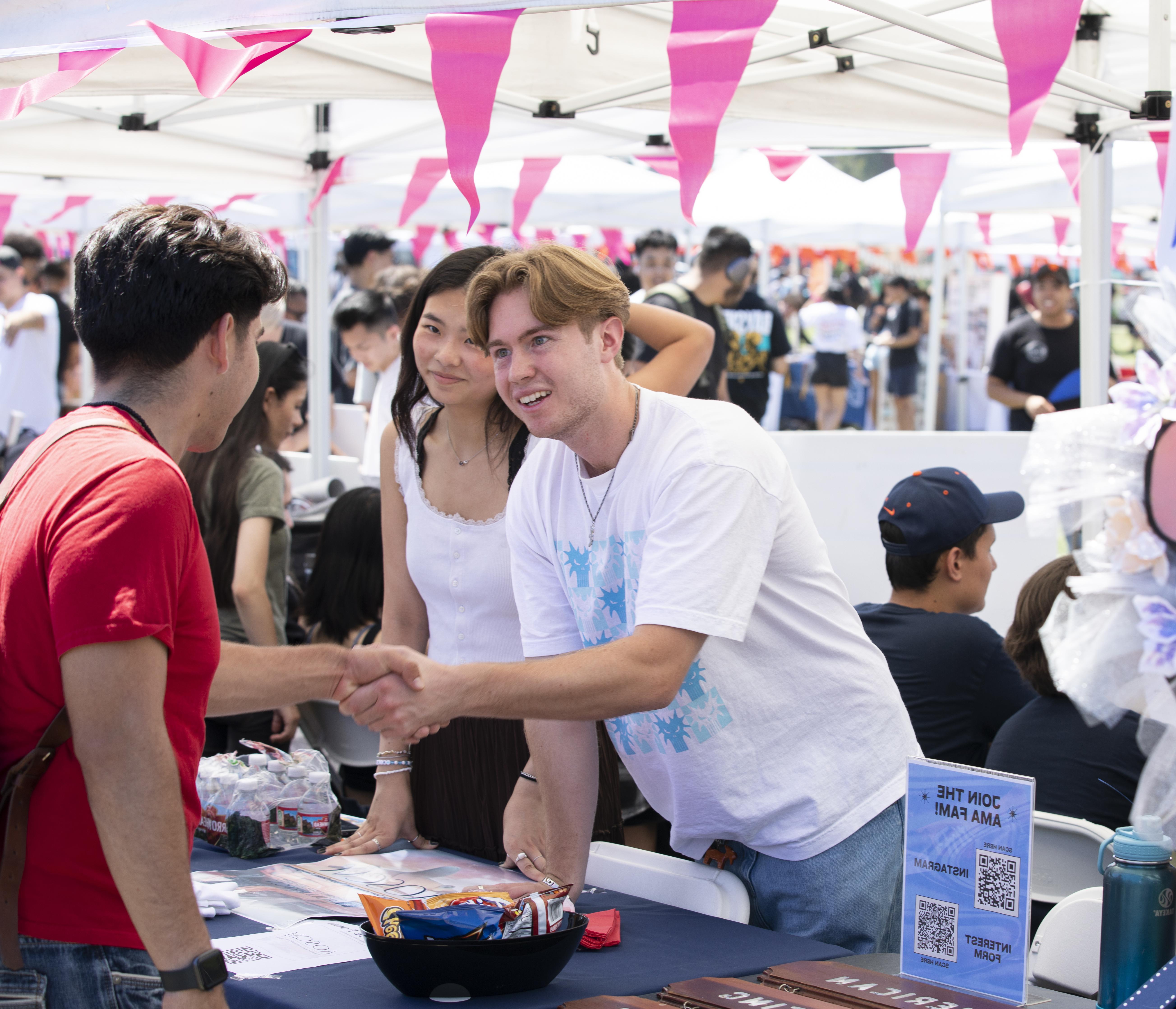 Students with the American Marketing Association meet a prospective club member at Discoverfest in Fall 2023. They shake each other's hands as they meet one another.